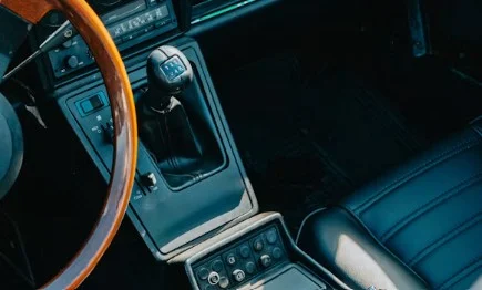 Close-up of a car interior featuring a wood-rimmed steering wheel, manual transmission gear shift, and black leather seats, with controls and buttons visible near the center console—a classic setup perfect for cruising through Twin Falls or exploring the scenic roads of Magic Valley.