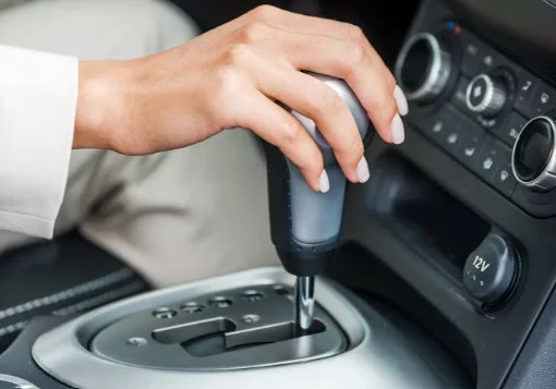 A person’s hand is shifting the transmission gear lever of an automatic car. The dashboard, control buttons, and gear positions are visible—perhaps en route through the bench-to-canyon geography of West Pocatello.