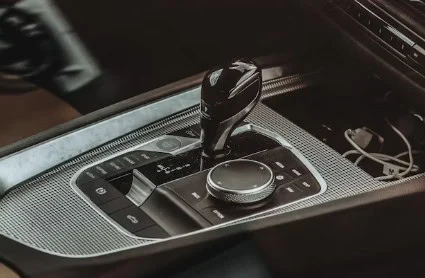 Close-up of a modern car’s center console featuring a gear shifter, control dial, buttons, and visible charging cables in a storage compartment—perfect for road trips through Ute Pass or spotting transmission warning signs on the way to Woodland Park.