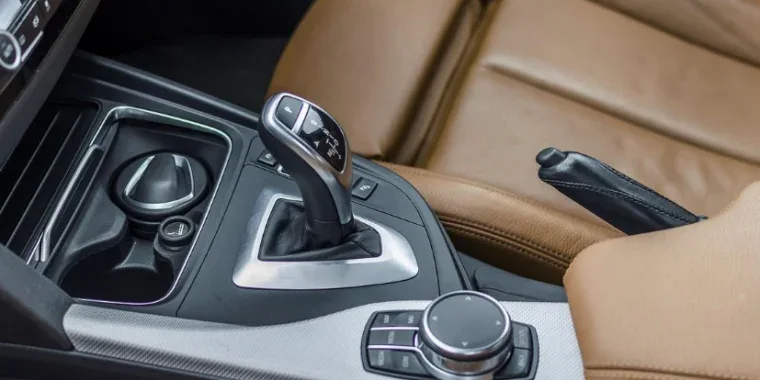 Close-up of a car’s center console in the heart of Dairy Country near Jerome, Idaho, showing a leather seat, gear shifter for the transmission, control dial, cup holder, and parking brake lever.