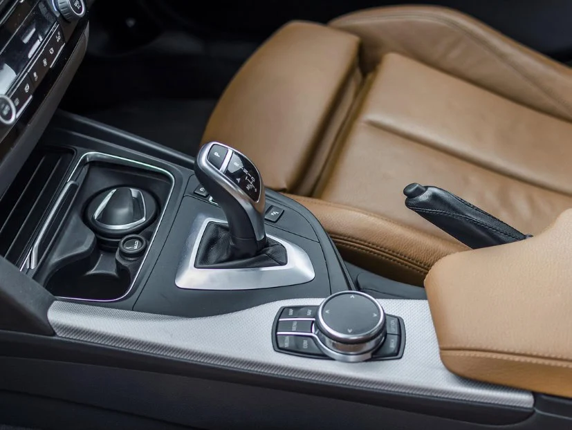 Close-up of a car’s center console in the heart of Dairy Country near Jerome, Idaho, showing a leather seat, gear shifter for the transmission, control dial, cup holder, and parking brake lever.