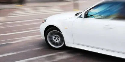 White sedan car quickly turning on a city street, with motion blur visible on the wheels and background—a scenario that Littleton drivers might encounter, especially if they start noticing transmission warning signs or potential transmission problems.