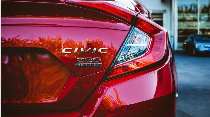 Close-up of the rear of a red Honda Civic 220 Turbo parked outside a Honda dealership, showing the model badge and tail light—a reminder of the importance of regular vehicle maintenance like brake system service at trusted centers such as Grease Monkey Rexburg.