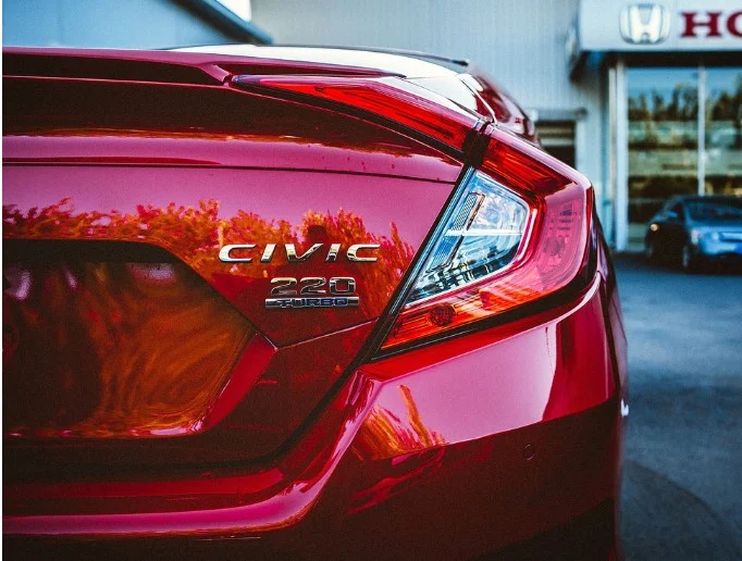Close-up of the rear of a red Honda Civic 220 Turbo parked outside a Honda dealership, showing the model badge and tail light—a reminder of the importance of regular vehicle maintenance like brake system service at trusted centers such as Grease Monkey Rexburg.