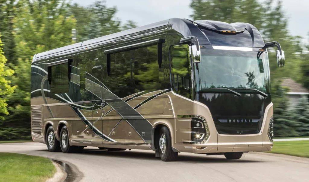 A large, modern luxury motorhome with black and beige detailing drives on a curved road surrounded by greenery, showcasing the importance of regular vehicle maintenance. Whether you’re planning an extended journey or just passing through the area, services like Grease Monkey Rexburg can help ensure your travels remain smooth and safe with essential brake system service.