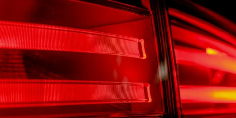Close-up of illuminated red car tail lights at night, showing horizontal light strips and reflective surfaces—reminding drivers in Laramie, Wyoming of the importance of regular brake inspection and professional brake service.