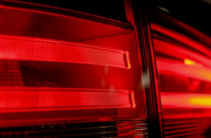 Close-up of illuminated red car tail lights at night, showing horizontal light strips and reflective surfaces—reminding drivers in Laramie, Wyoming of the importance of regular brake inspection and professional brake service.