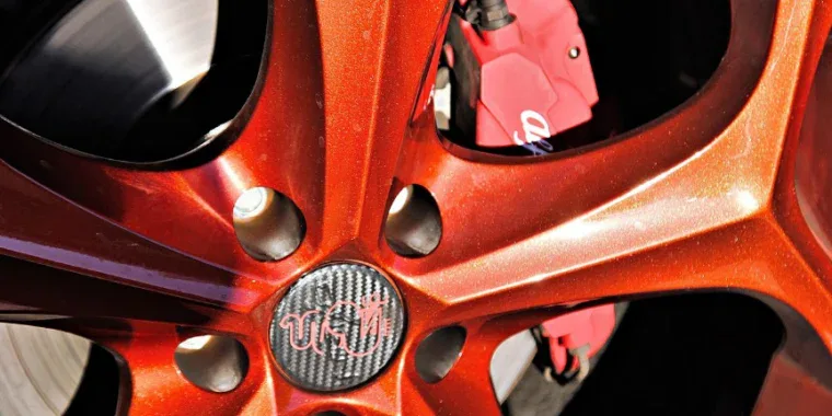 Close-up of a metallic red car wheel rim with a visible brake caliper and a carbon fiber-style center cap featuring a logo, showcasing the importance of maintaining your brake system with regular service—essential for drivers in Pocatello, Idaho.