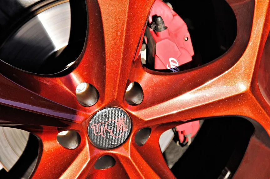 Close-up of a metallic red car wheel rim with a visible brake caliper and a carbon fiber-style center cap featuring a logo, showcasing the importance of maintaining your brake system with regular service—essential for drivers in Pocatello, Idaho.