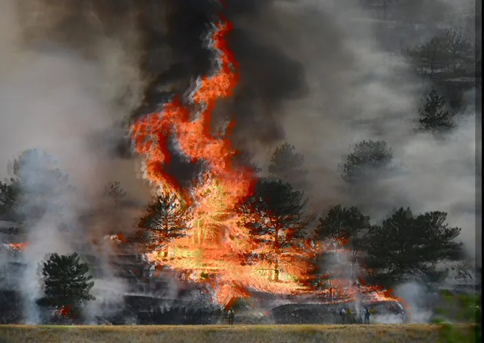 Wildfire engulfs pine trees, with large flames and thick black smoke rising into the sky near Elizabeth, Colorado; firefighters are visible at the bottom of the image, battling the blaze just miles from local brake service and brake inspection centers.