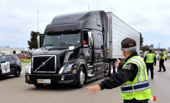 Police officers direct a black semi-truck during an INL Commute roadside inspection near Idaho Falls. Several officers and patrol vehicles are visible in the background, ensuring safe transmission of traffic through the area.