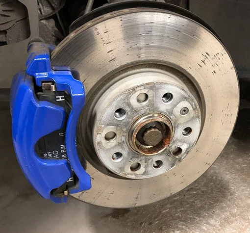 A close-up of a car’s brake disc and blue brake caliper, showing some rust on the central hub and surface wear on the disc—a clear reminder of the importance of regular vehicle maintenance and timely brake system service, especially for drivers in Twin Falls Idaho.