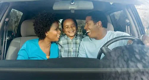 A man, woman, and child sit in the front seat of a car, smiling and laughing together as they cruise through West Pocatello, enjoying the journey from bench-to-canyon geography.