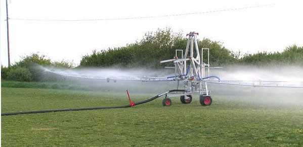A machine with spray arms is irrigating a grassy field near Kimberly, Idaho, releasing water from multiple nozzles while connected to a large hose.