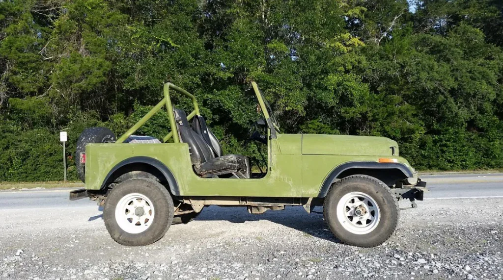 Green open-top Jeep parked on gravel beside a road, with dense trees in the background—a common sight for adventurous Littleton drivers who should always be aware of transmission warning signs and potential transmission problems when traveling off the beaten path.