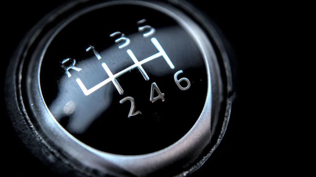 Close-up of a manual car gear shift knob showing six forward gears and reverse, labeled with white numbers and lines—a familiar sight for Aurora Colorado drivers navigating I-225, especially when a transmission emergency arises.