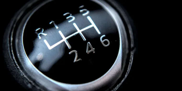 Close-up of a manual car gear shift knob showing six forward gears and reverse, labeled with white numbers and lines—a familiar sight for Aurora Colorado drivers navigating I-225, especially when a transmission emergency arises.