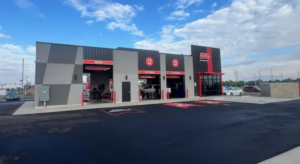 A modern drive-through oil change service center with three service bays, red and black accents, and a clear sky overhead, conveniently located in West Pocatello amidst striking Bench-to-Canyon geography, also offering quick transmission services.