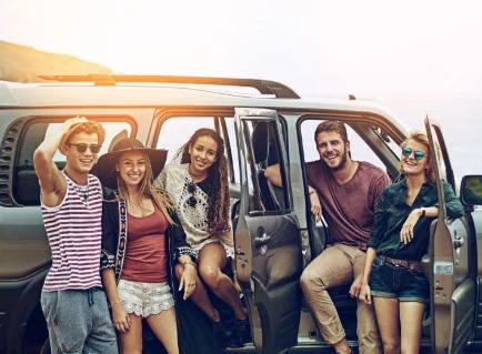 Five young adults stand by an SUV with open doors, smiling at the camera. The group appears relaxed, dressed in casual summer clothes, with an outdoor setting in the background—perhaps enjoying a scenic road trip near Idaho Falls after taking care of some routine vehicle maintenance.