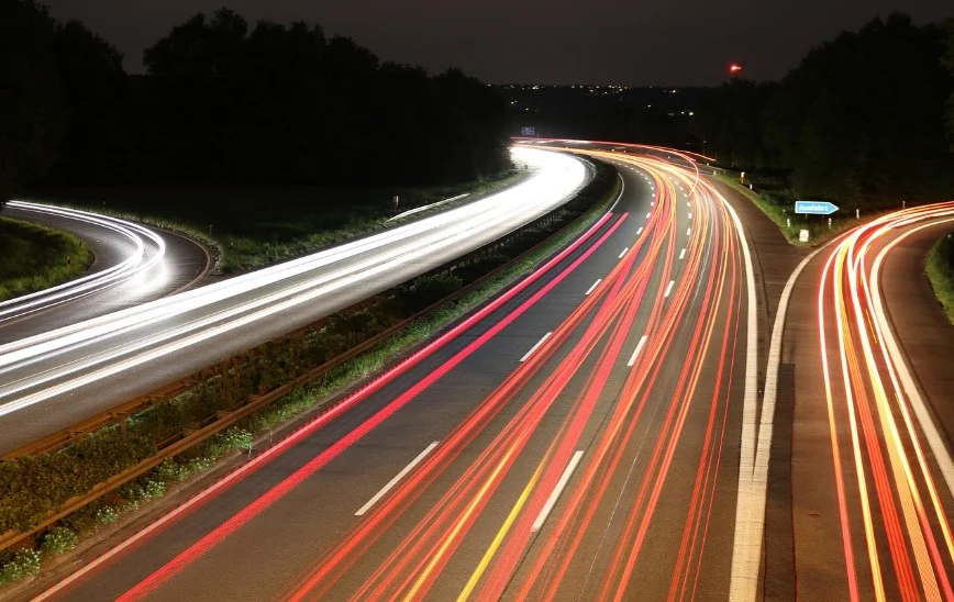Long-exposure photo of a highway at night shows white and red light trails from vehicles, with trees lining both sides of the road—a striking reminder of how vital vehicle maintenance and dependable brake system repair are for safe journeys, whether you’re cruising through the city or visiting Grease Monkey Rexburg.