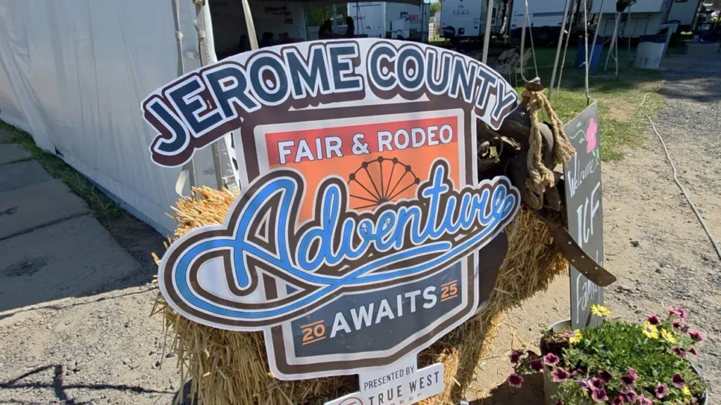 Sign reading “Jerome County Fair & Rodeo Adventure Awaits 2025” displayed on straw with flowers and a hat nearby at an outdoor event in Jerome, Idaho, where local traditions are celebrated and even the parade floats look like they’ve been serviced regularly.
