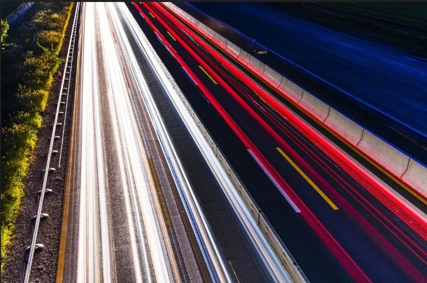 Long-exposure photo of a highway at night near Pocatello, Idaho, showing white and red light trails from fast-moving vehicles in opposite directions—a dynamic reminder of how a well-maintained brake system and regular service are essential for safe travels.