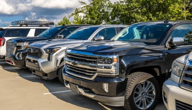 Four pickup trucks are parked side by side in an outdoor parking lot under a partly cloudy sky with trees in the background—a typical scene for Jerome Idaho drivers navigating dairy country, where a reliable transmission is essential.