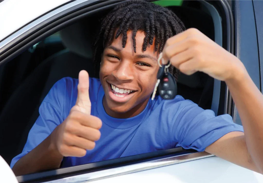 Smiling young person sitting in a car in Twin Falls, Idaho, holds up car keys and gives a thumbs up through the open window—ready to hit the road with confidence after a thorough brake system check.