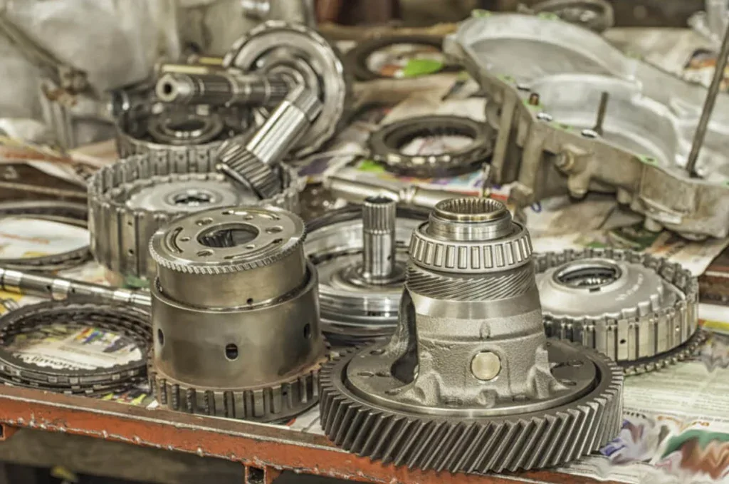 Various disassembled metal transmission and automotive gearbox parts and gears are arranged on a workbench covered with newspaper in a workshop setting, reflecting the skilled craftsmanship found in Magic Valley.