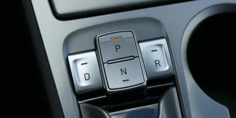 Close-up of a car’s electronic gear selector with buttons labeled P, R, N, and D, located on the center console next to a cup holder.