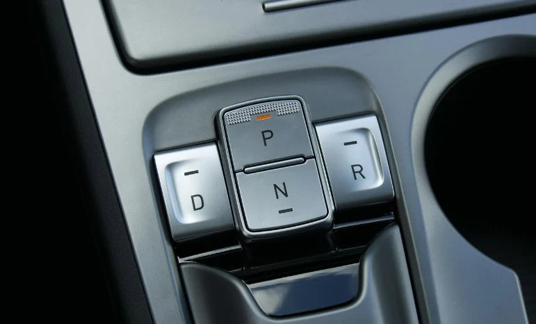 Close-up of a car’s electronic gear selector with buttons labeled P, R, N, and D, located on the center console next to a cup holder.