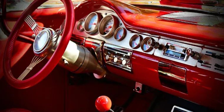 Close-up view of a classic car’s red interior showing the steering wheel, transmission gear shift, dashboard with round dials, and vintage radio—reminiscent of drives down the fastest-growing streets in Kimberly Idaho.