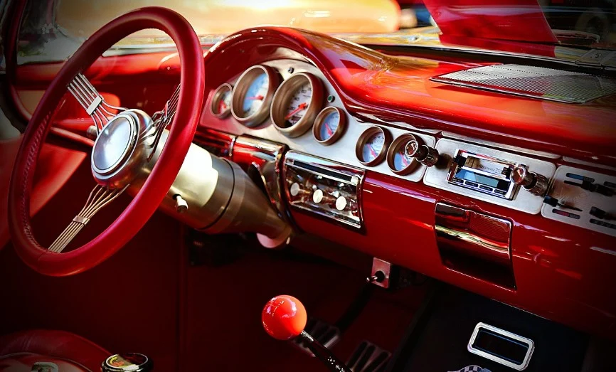Close-up view of a classic car’s red interior showing the steering wheel, transmission gear shift, dashboard with round dials, and vintage radio—reminiscent of drives down the fastest-growing streets in Kimberly Idaho.