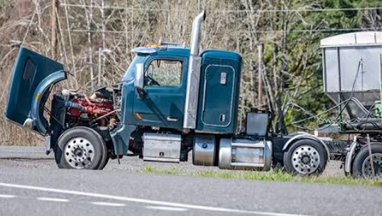 A blue semi-truck, commonly used as one of the Elizabeth Colorado ranch vehicles, is parked on the roadside with its hood open, exposing the engine—possibly due to transmission problems. Trees and power lines are visible in the background.