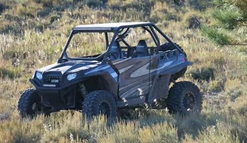 A black off-road utility vehicle with large tires is parked on grassy terrain under daylight, ready to tackle the rugged landscapes near Kimberly Idaho.