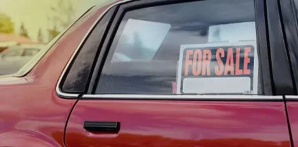 A red car with a “For Sale” sign displayed in the back window, parked outdoors in Idaho Falls. This well-maintained vehicle has recently had its brake system repair completed, ensuring reliable performance for its next owner.