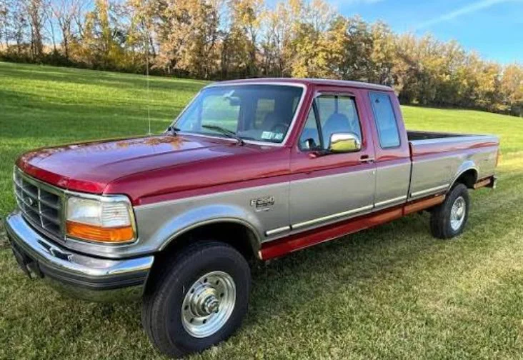A two-tone red and silver Ford F-250 pickup truck is parked on grass in Elizabeth, Colorado, with trees and a clear sky in the background—perfect for a brake inspection or reliable brake service.