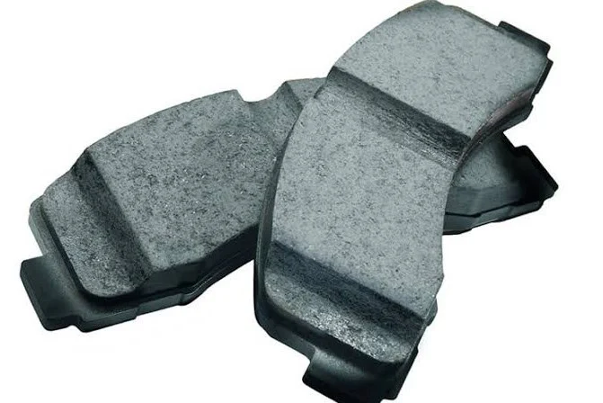 Two automotive brake pads are placed next to each other on a plain background, showing their friction surfaces and edges—an essential part of any vehicle maintenance routine in Woodland Park, Colorado, especially when considering comprehensive brake system service.
