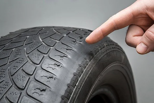 A hand points to a worn, damaged section of a black car tire, showing visible cracks and uneven tread—signs that highlight the importance of regular vehicle maintenance in Woodland Park, Colorado, and indicate the need for a replacement.