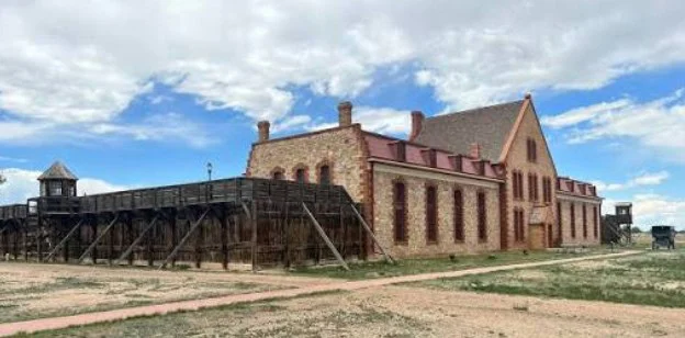 Historic stone building with red roof and wooden walkway, under a partly cloudy sky, on a barren landscape near Laramie, Wyoming—a scene where history meets the present, much like how proper car maintenance, such as replacing your cabin air filter, keeps your journey smooth across these timeless terrains.