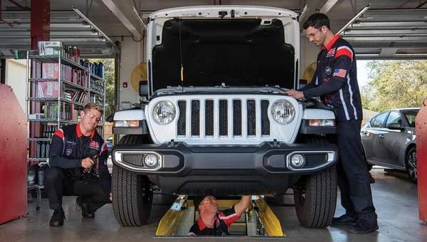 Three Grease Monkey technicians service a white Jeep inside an open service bay.