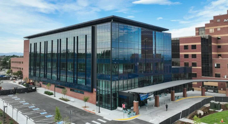 A modern, four-story glass and brick building with accessible parking spaces and a covered entrance, situated next to a larger brick facility under a partly cloudy sky—perfect for anyone in Littleton, Colorado seeking professional car maintenance services such as cabin air filter replacement.