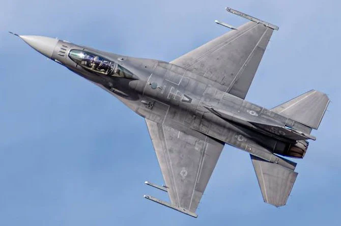 A gray military fighter jet is flying with its wings angled upward against a clear blue sky above Aurora, Colorado, not far from Buckley Space Force Base.
