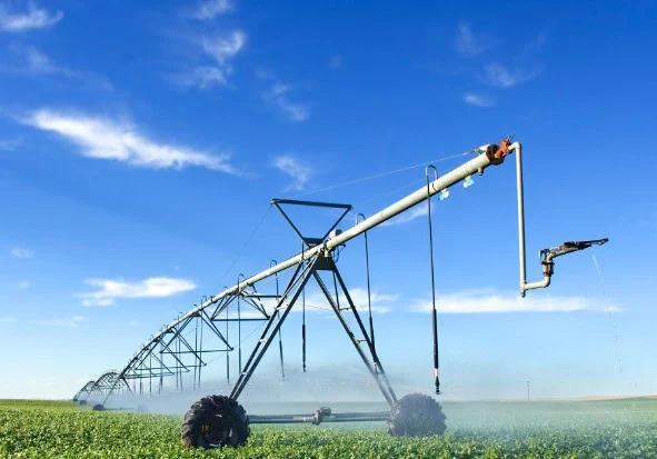A center pivot irrigation system sprays water over a green crop field under a blue sky with scattered clouds near Rexburg Idaho.