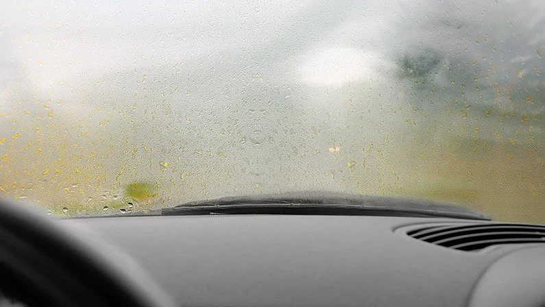 View from inside a car looking through a windshield covered in condensation, with the dashboard and part of the steering wheel visible—reminding drivers in Rexburg Idaho of the importance of regular car maintenance, such as checking or replacing the cabin air filter for clear visibility.