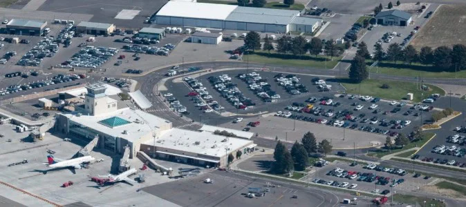 Aerial view of Idaho Falls airport terminal with two airplanes at gates, adjacent parking lots filled with cars, and surrounding buildings and roads—offering a glimpse into the busy travel hub that serves Yellowstone traffic.