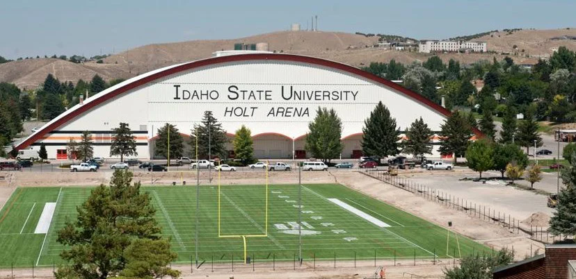 View of Holt Arena at Idaho State University with a green football field in the foreground and hills in the background—a picturesque scene that highlights some of the unique landscapes you might encounter while traveling through Idaho for car maintenance or picking up essential parts like a cabin air filter, whether you’re coming from Rexburg, Idaho or beyond.