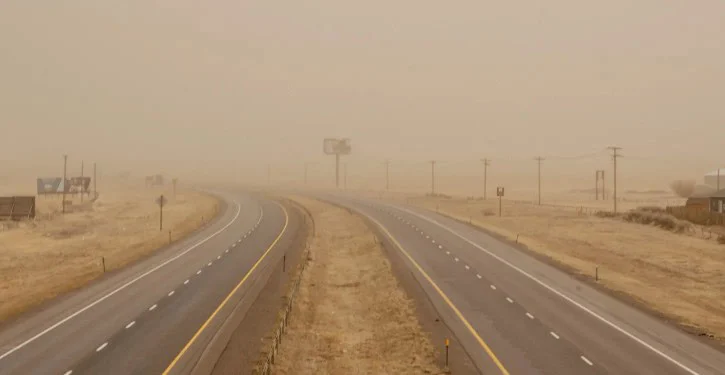 A deserted highway near Laramie, Wyoming is shown under heavy dust or fog, limiting visibility. The landscape is dry, with brown grass and utility poles lining the road—a stark reminder of how important car maintenance, like regularly changing your cabin air filter, can be in such conditions.