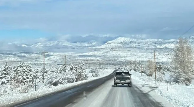 A truck drives down a snow-covered road near Rexburg, Idaho, with snow blanketing the surrounding landscape and mountains in the background.