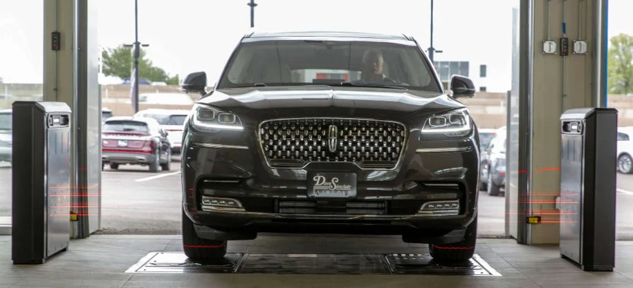 A black SUV faces forward inside a garage in Idaho Falls, positioned between two Quick Check alignment scanning machines, with cars and a building visible outside.